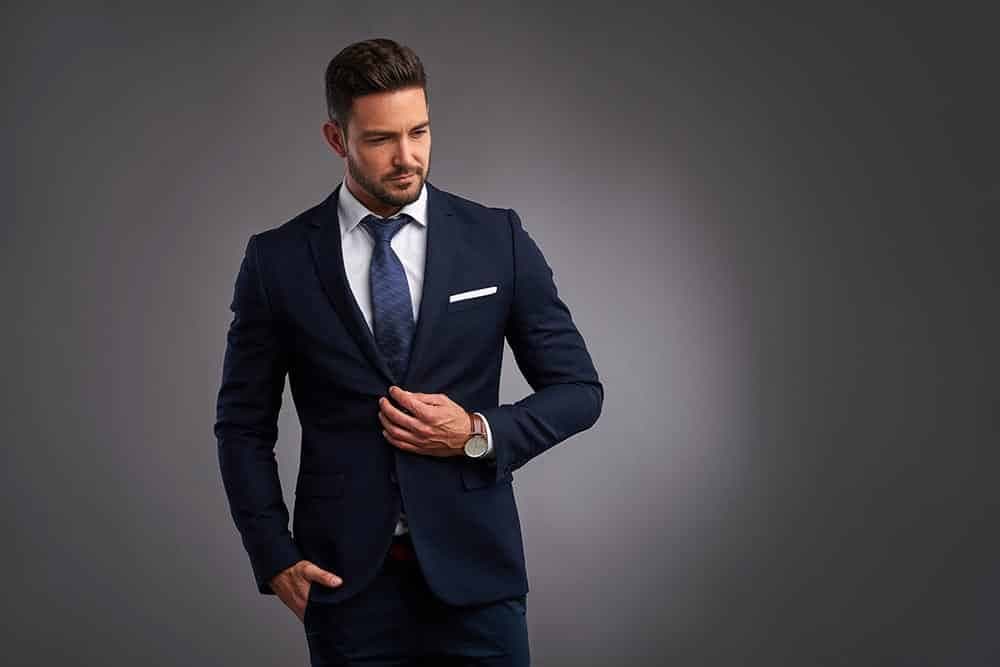 Man in a navy suit fastening his jacket