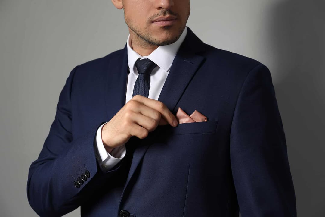 Man in a navy suit adjusting his pocket square
